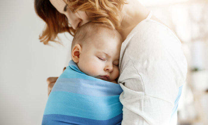 Precious little newborn boy having deep sleep at day on mother chest in blue baby sling. mom kissing baby head and feeling relaxed and delight. family concept.